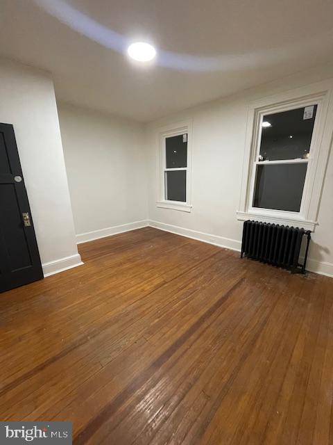 empty room with dark wood-style floors, radiator, and baseboards