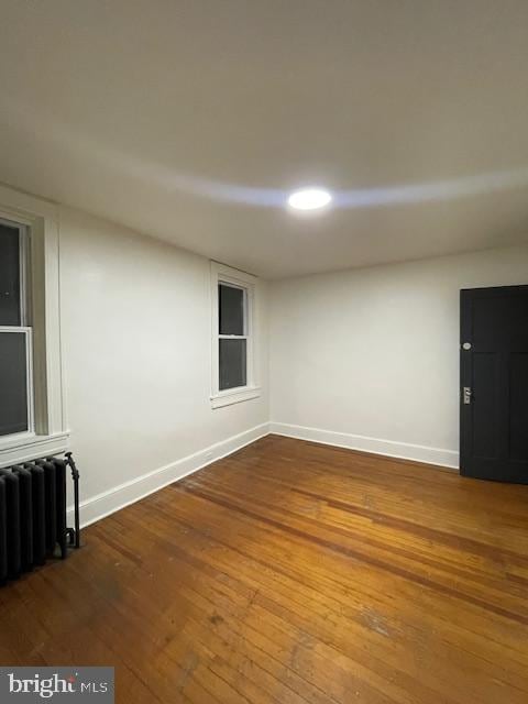 unfurnished room featuring baseboards, wood-type flooring, and radiator