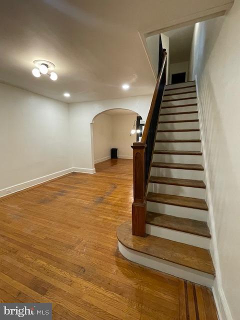 stairway with recessed lighting, baseboards, arched walkways, and wood finished floors