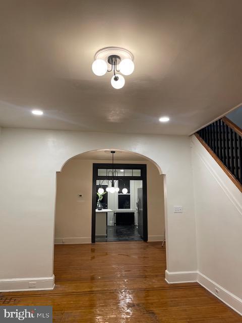 unfurnished dining area with wood finished floors, arched walkways, and baseboards