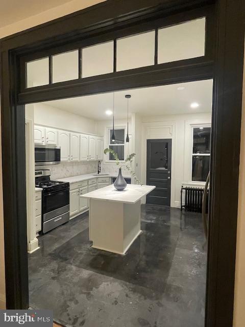 kitchen with a sink, white cabinetry, concrete floors, appliances with stainless steel finishes, and light countertops