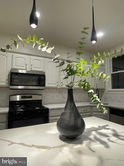 interior details with decorative backsplash, stainless steel microwave, white cabinetry, dishwashing machine, and gas range