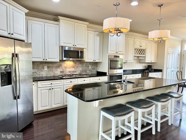 kitchen with a kitchen island with sink, white cabinets, stainless steel appliances, and decorative light fixtures