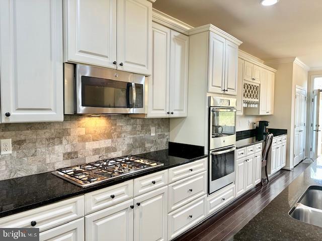 kitchen featuring dark stone counters, white cabinetry, stainless steel appliances, and ornamental molding