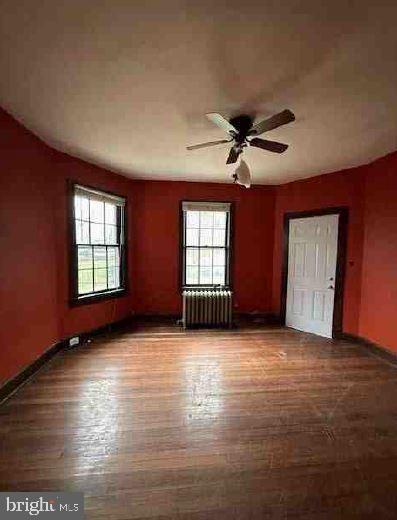 empty room featuring radiator heating unit, hardwood / wood-style flooring, and ceiling fan