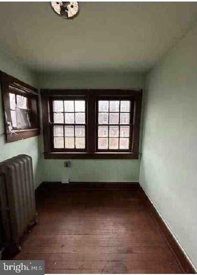 empty room with dark hardwood / wood-style floors, plenty of natural light, and radiator heating unit