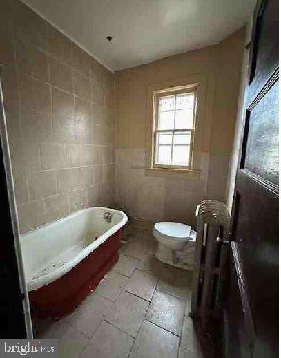 bathroom featuring a bathing tub, toilet, and tile walls