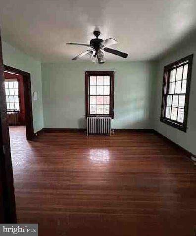 unfurnished room with dark hardwood / wood-style flooring, a wealth of natural light, radiator heating unit, and ceiling fan