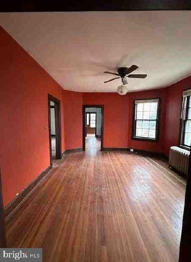 spare room featuring wood-type flooring, radiator, and ceiling fan