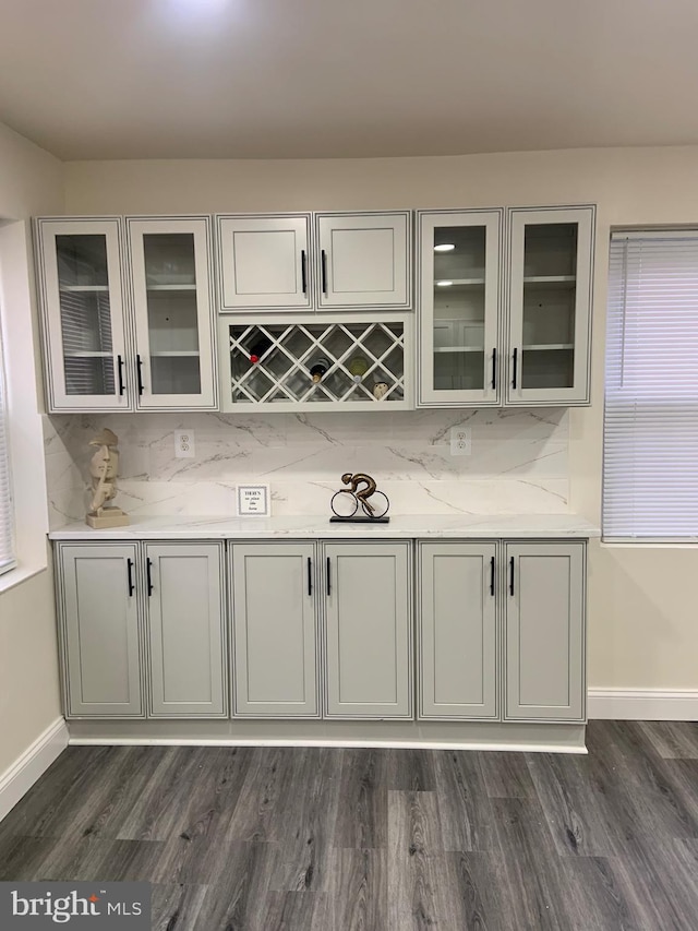 bar featuring light stone countertops, tasteful backsplash, and dark wood-type flooring