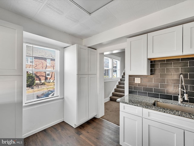 kitchen featuring backsplash, dark wood-type flooring, white cabinets, sink, and dark stone countertops