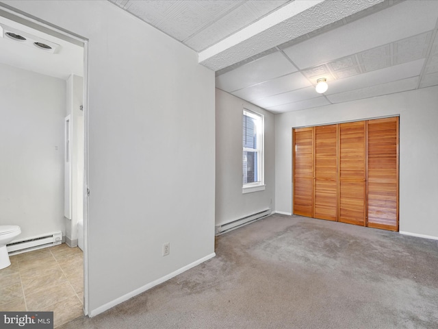 unfurnished bedroom featuring baseboard heating, a closet, a drop ceiling, and light carpet