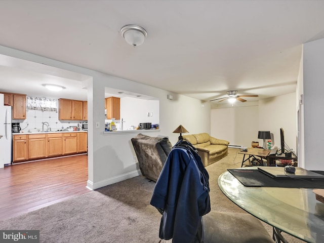 carpeted living room featuring baseboard heating, ceiling fan, and sink