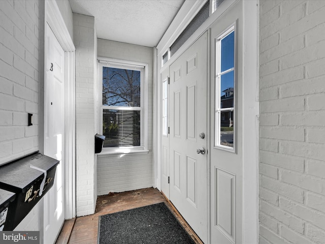 doorway to outside featuring a textured ceiling and brick wall