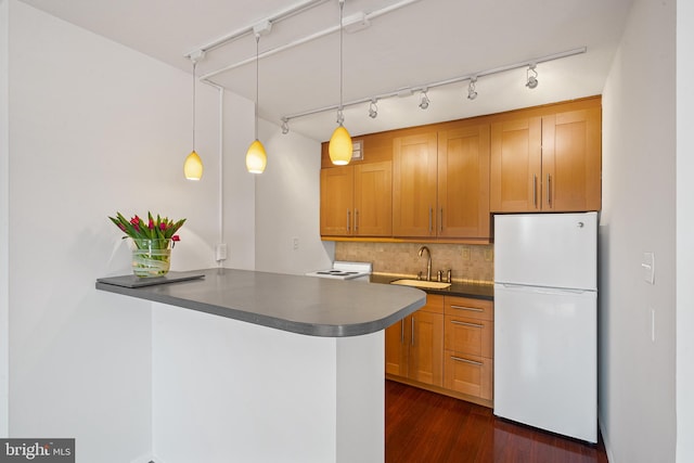 kitchen with dark countertops, backsplash, freestanding refrigerator, a sink, and a peninsula