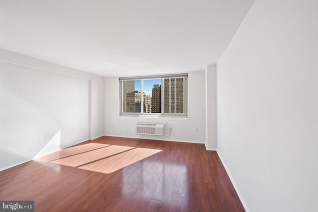 spare room featuring a wall unit AC, baseboards, and wood finished floors