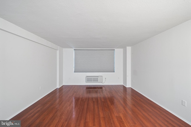 unfurnished living room with an AC wall unit, a textured ceiling, baseboards, and wood finished floors