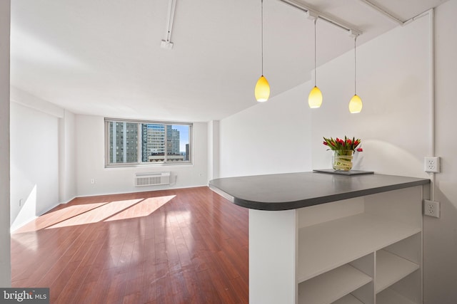 kitchen with hardwood / wood-style flooring, a wall mounted air conditioner, hanging light fixtures, dark countertops, and rail lighting
