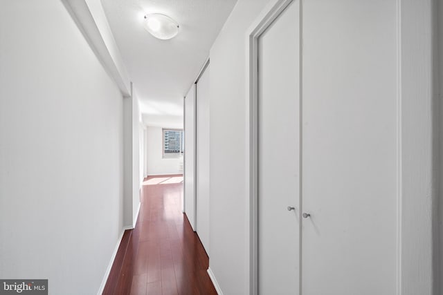 hall featuring a textured ceiling, dark wood-style flooring, and baseboards