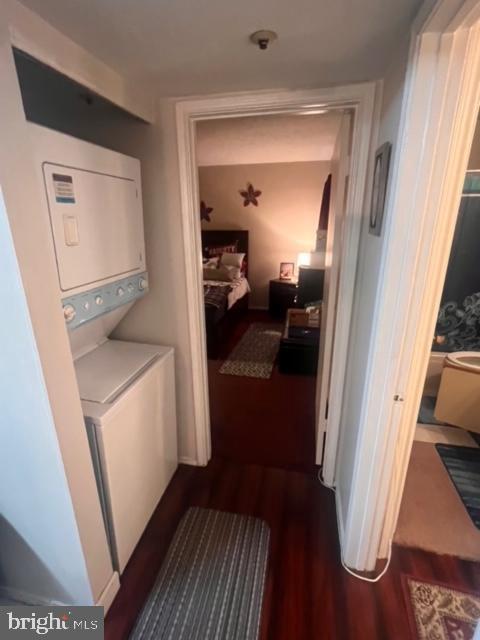 laundry area with dark wood-type flooring and stacked washer and clothes dryer