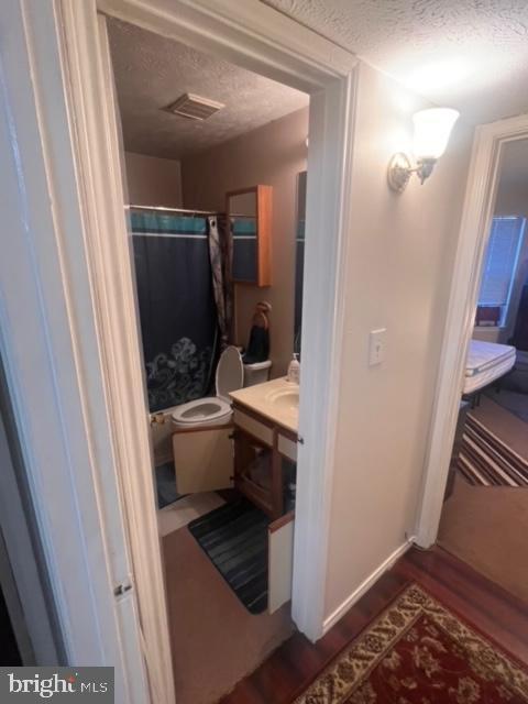 bathroom featuring a textured ceiling, hardwood / wood-style flooring, toilet, and curtained shower