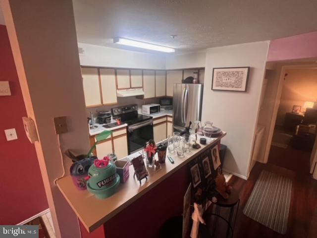 kitchen with black electric range oven, kitchen peninsula, and stainless steel refrigerator