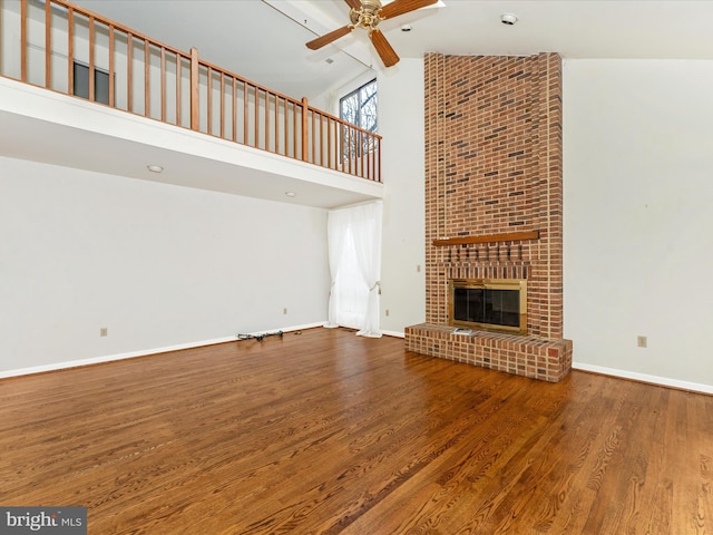 unfurnished living room with wood-type flooring, high vaulted ceiling, ceiling fan, and a brick fireplace