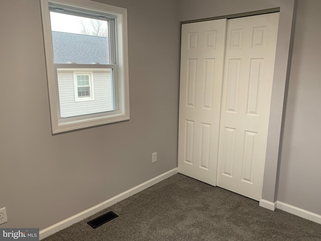 unfurnished bedroom with dark colored carpet and a closet