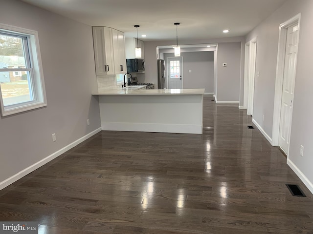 kitchen with kitchen peninsula, appliances with stainless steel finishes, decorative light fixtures, white cabinets, and plenty of natural light