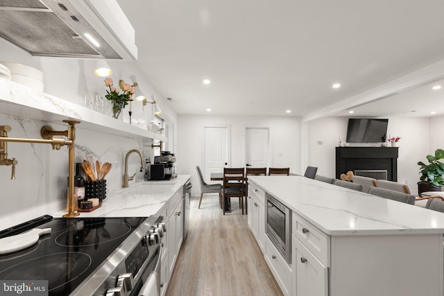 kitchen featuring a center island, white cabinets, light wood-type flooring, light stone counters, and stainless steel appliances