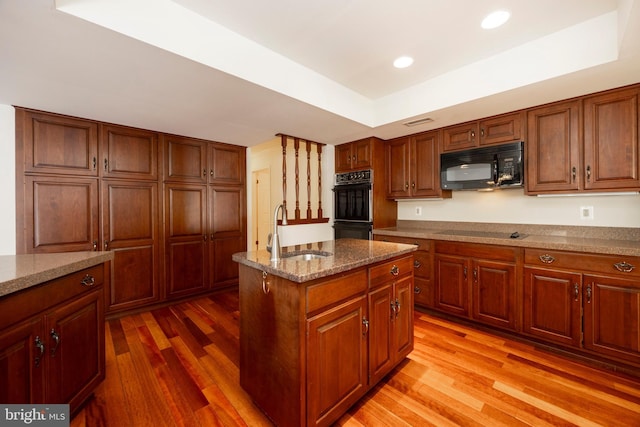 kitchen with sink, hardwood / wood-style flooring, a center island, black appliances, and light stone countertops