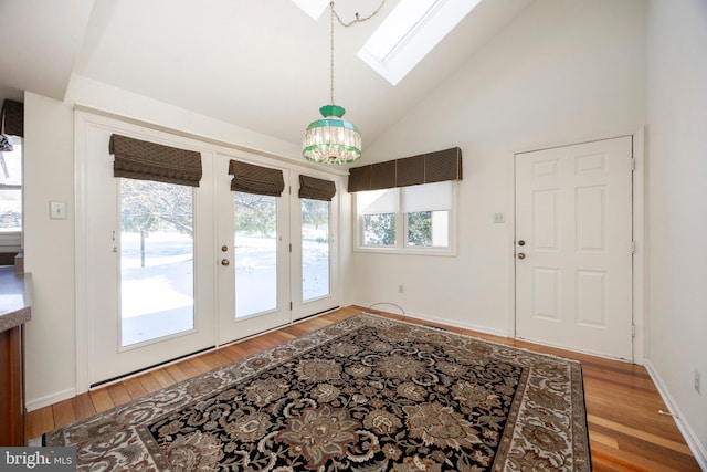 doorway with hardwood / wood-style floors, high vaulted ceiling, and a skylight