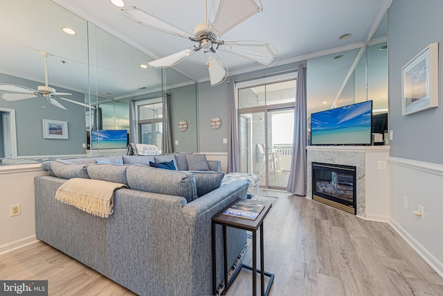 living room featuring light wood-type flooring, ceiling fan, ornamental molding, and a premium fireplace