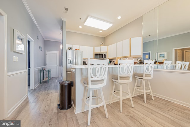 kitchen featuring kitchen peninsula, stainless steel appliances, light hardwood / wood-style flooring, white cabinets, and a breakfast bar area