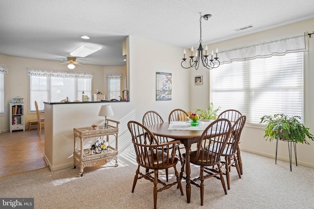 carpeted dining area featuring a textured ceiling and ceiling fan with notable chandelier