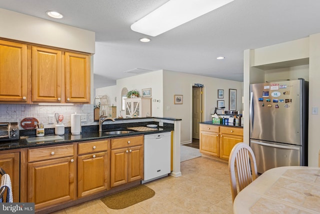 kitchen featuring sink, tasteful backsplash, dark stone countertops, stainless steel fridge, and white dishwasher