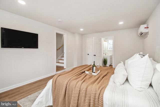 bedroom with hardwood / wood-style floors, connected bathroom, and a wall mounted AC