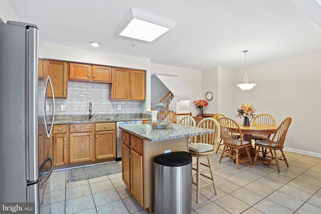 kitchen with light stone countertops, appliances with stainless steel finishes, pendant lighting, a center island, and a breakfast bar area