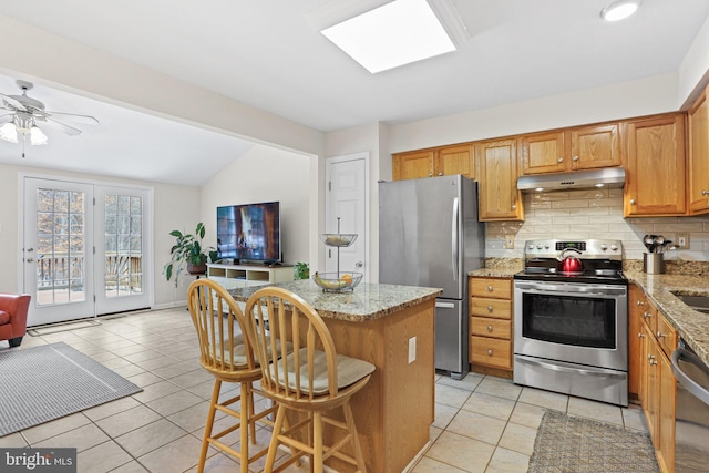 kitchen featuring light tile patterned floors, a kitchen breakfast bar, light stone counters, a kitchen island, and appliances with stainless steel finishes