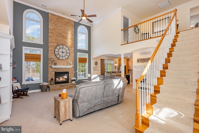 living room featuring a towering ceiling, ornate columns, ceiling fan, crown molding, and a stone fireplace