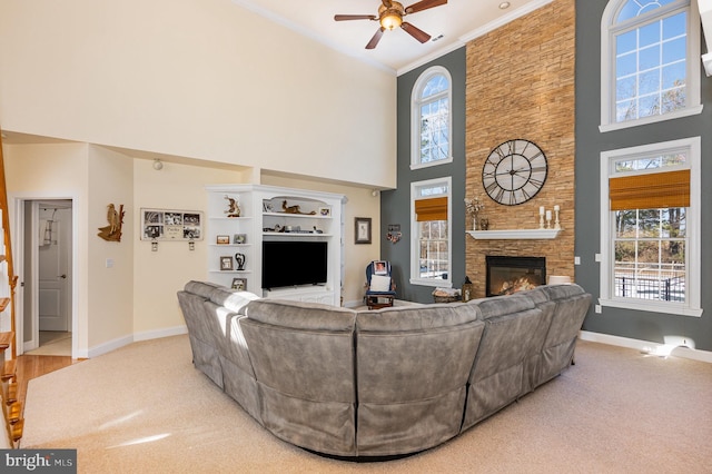 living room featuring a high ceiling, a fireplace, ceiling fan, and light colored carpet