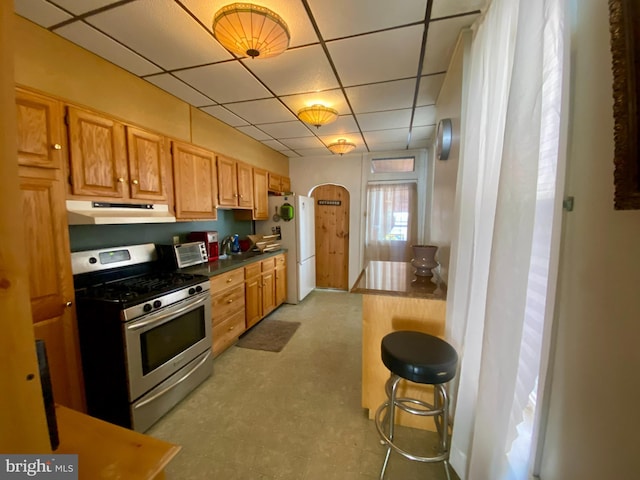 kitchen featuring white refrigerator, a kitchen bar, a drop ceiling, and stainless steel gas stove