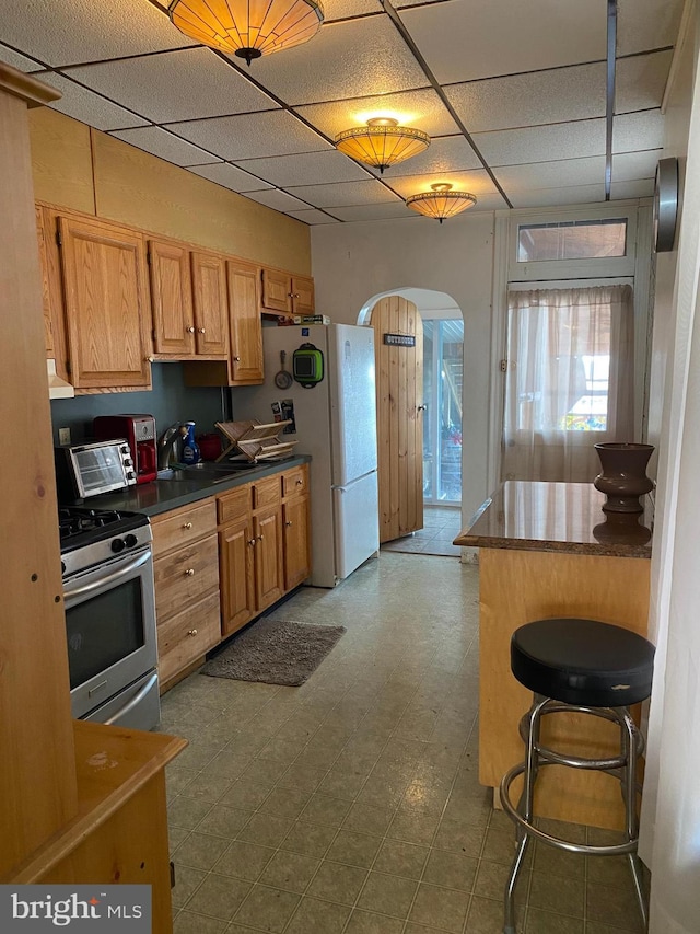 kitchen with stainless steel range with gas cooktop, a paneled ceiling, a kitchen breakfast bar, and white refrigerator