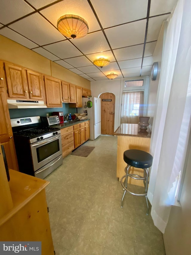 kitchen with stainless steel gas range oven, white fridge, a drop ceiling, and a kitchen bar