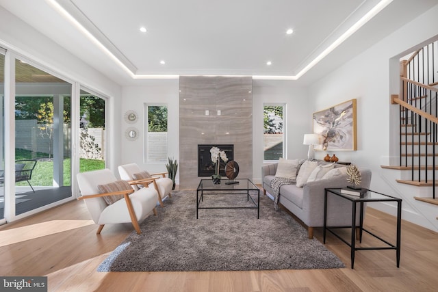 living room with a tray ceiling, light hardwood / wood-style flooring, and a tiled fireplace