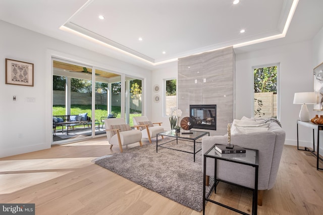 living room featuring a raised ceiling, a fireplace, and light hardwood / wood-style flooring