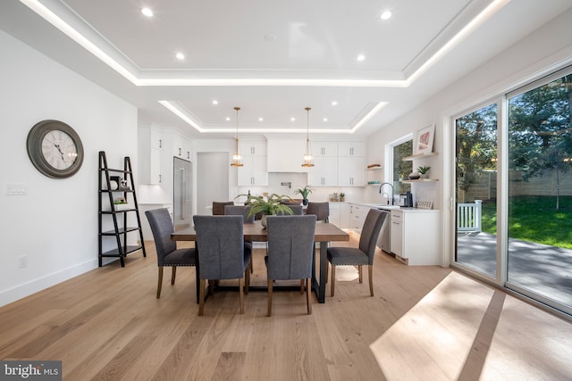 dining space featuring light hardwood / wood-style floors, a raised ceiling, and sink