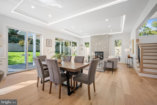 dining space with a raised ceiling, light wood-type flooring, and a tiled fireplace