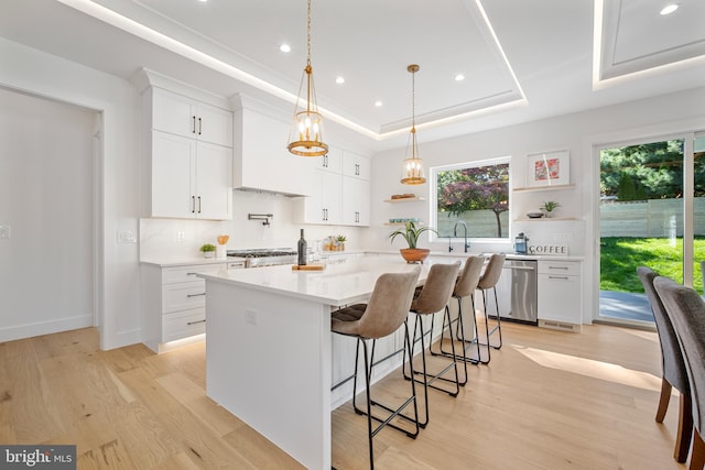 kitchen featuring a tray ceiling, white cabinetry, a kitchen bar, and stainless steel dishwasher