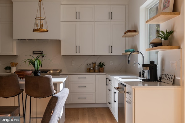 kitchen with pendant lighting, sink, light hardwood / wood-style flooring, tasteful backsplash, and white cabinetry